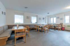 Geräumiger Pausenraum mit Holztischen, Eckbänken und mehreren Fenstern für Tageslicht.