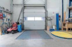 Innenansicht einer Garage oder Werkstatt mit großem Rolltor und Arbeitsbereich.