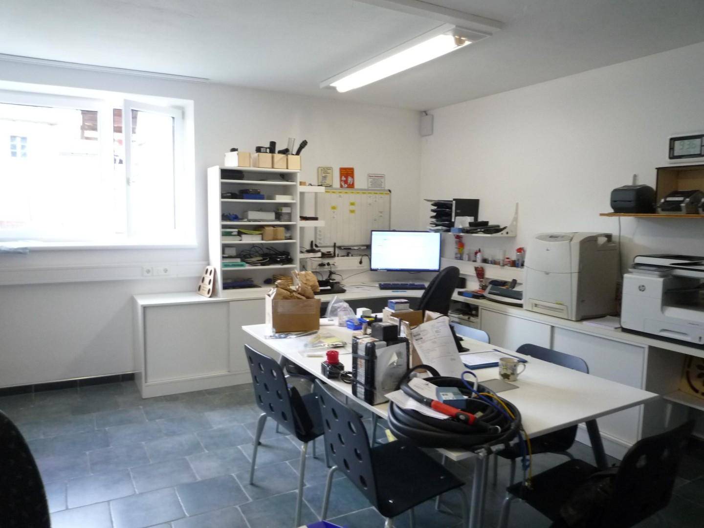 Helles Büro mit großem Fenster, Schreibtisch und Regalen für Arbeitsmaterialien.