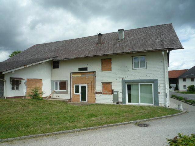 Vorderansicht des Wohnhauses mit Gartenfläche und modernen Fenstern unter bewölktem Himmel.