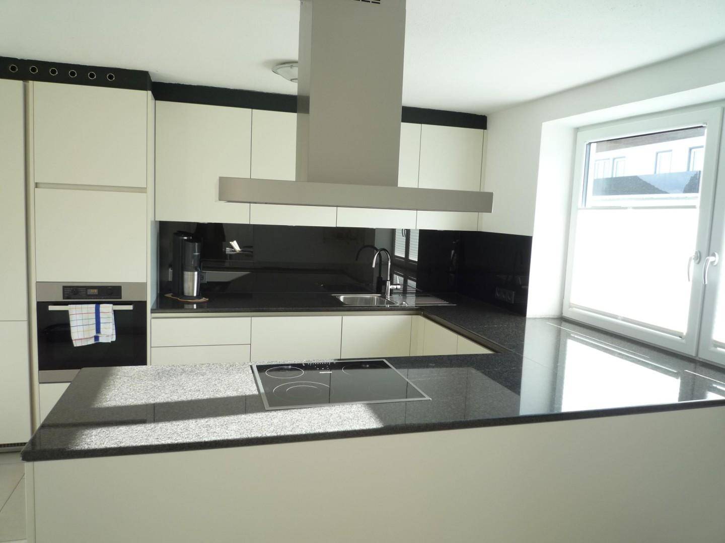 Moderne Küche mit schwarzen Granitarbeitsplatten, Induktionskochfeld und Dunstabzugshaube.