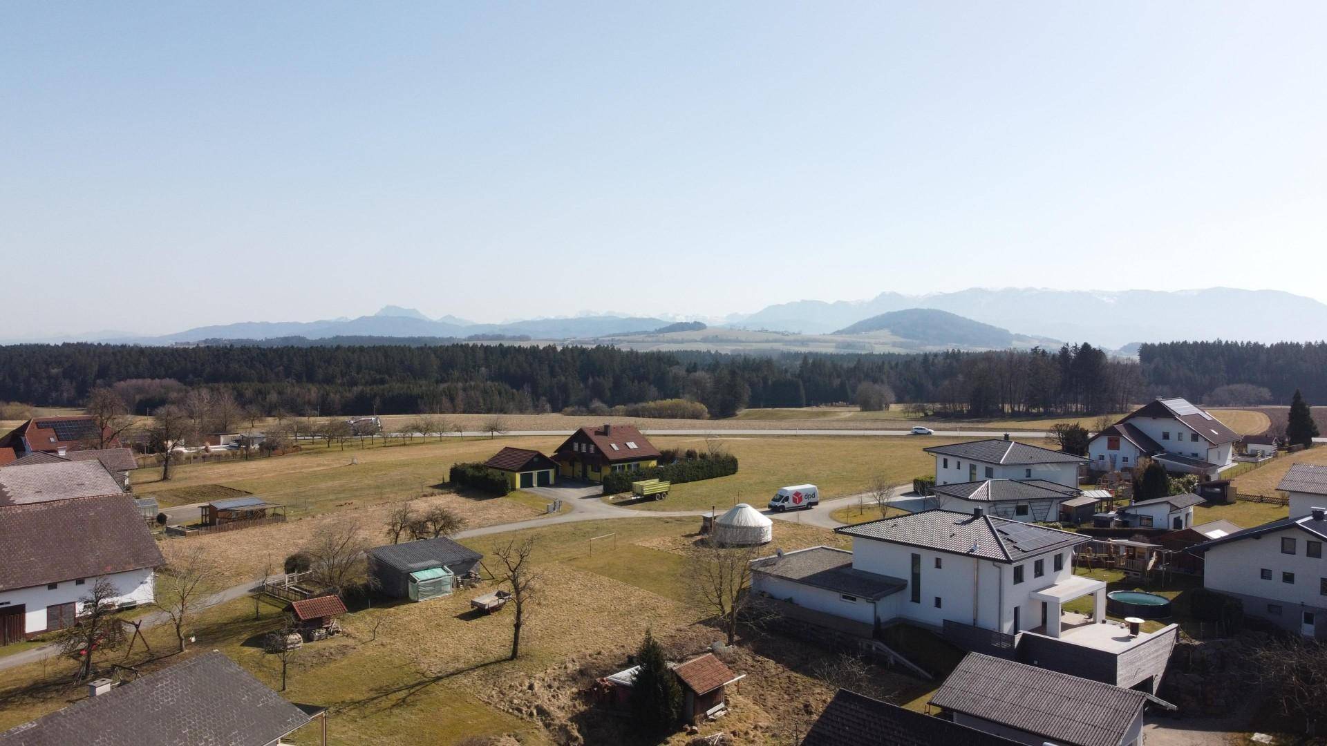 Weitläufige Luftaufnahme der ländlichen Umgebung mit Häusern und Bergen im Hintergrund.