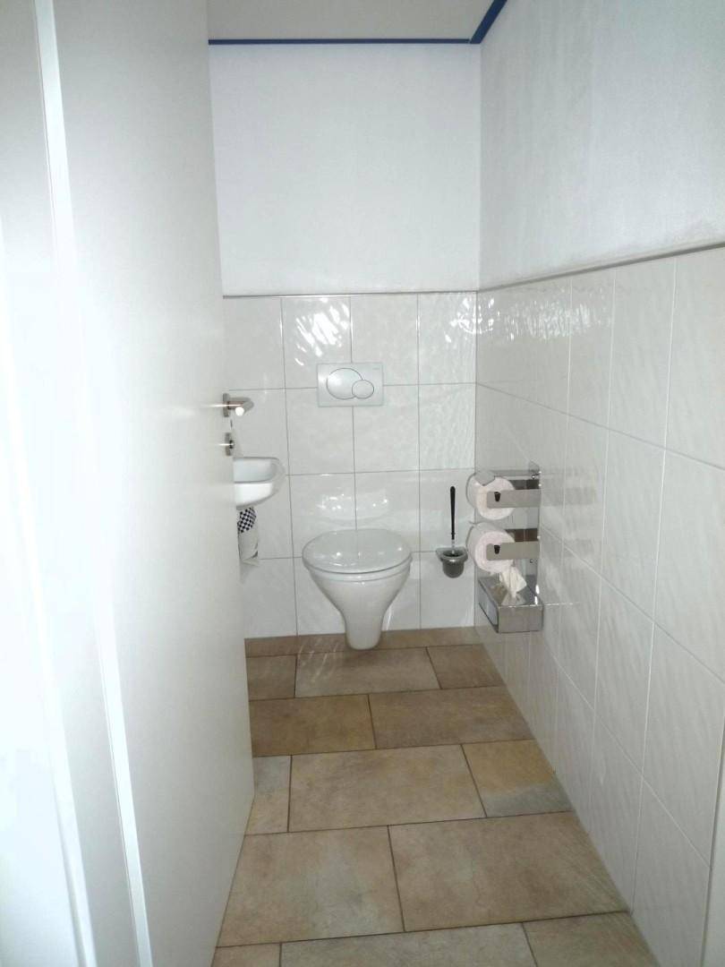 Kleines Gäste-WC mit Wand-WC, Waschbecken und hellen Fliesen.
