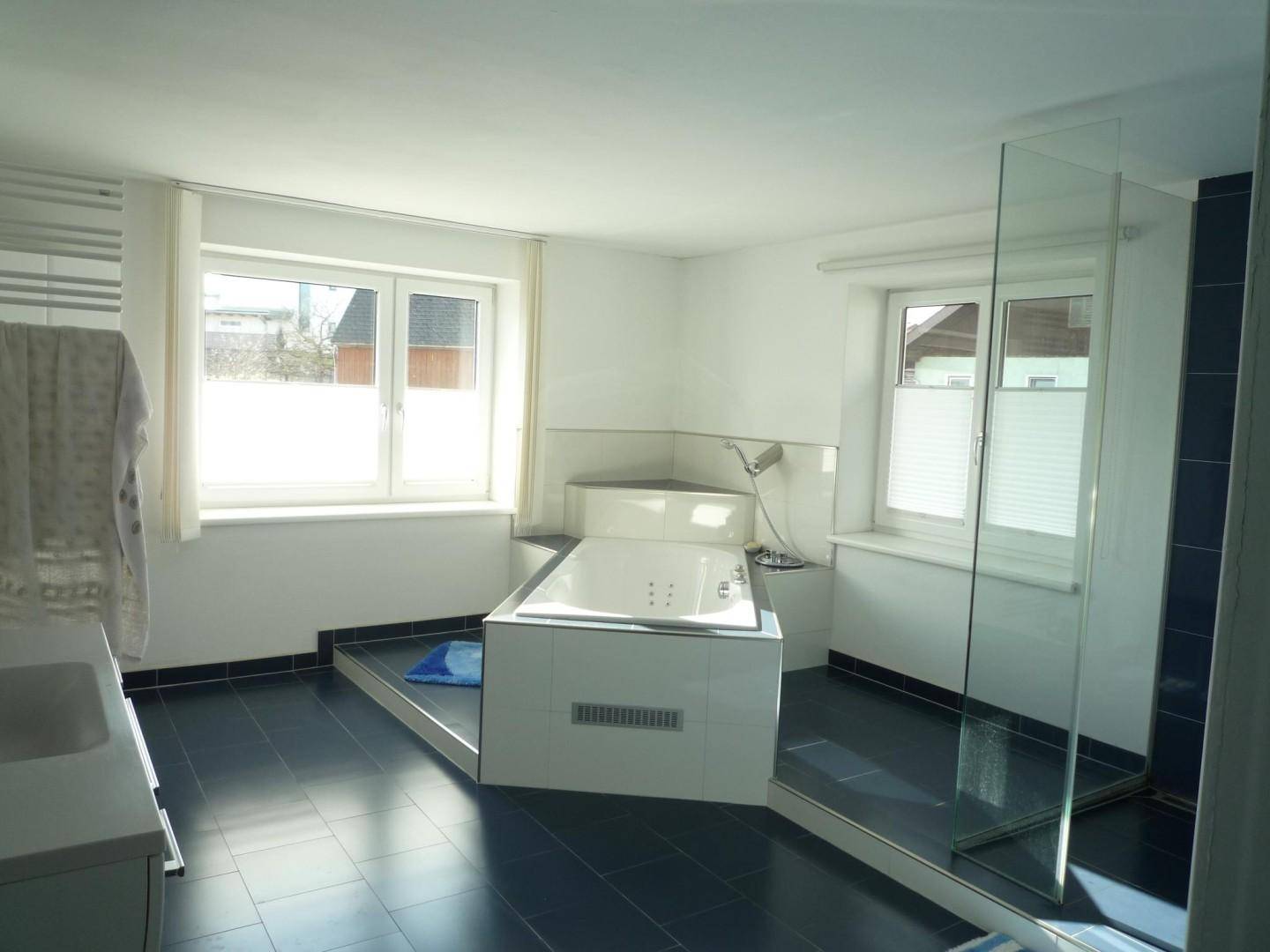 Geräumiges Badezimmer mit Whirlpool-Badewanne, großer Dusche und zwei Fenstern.