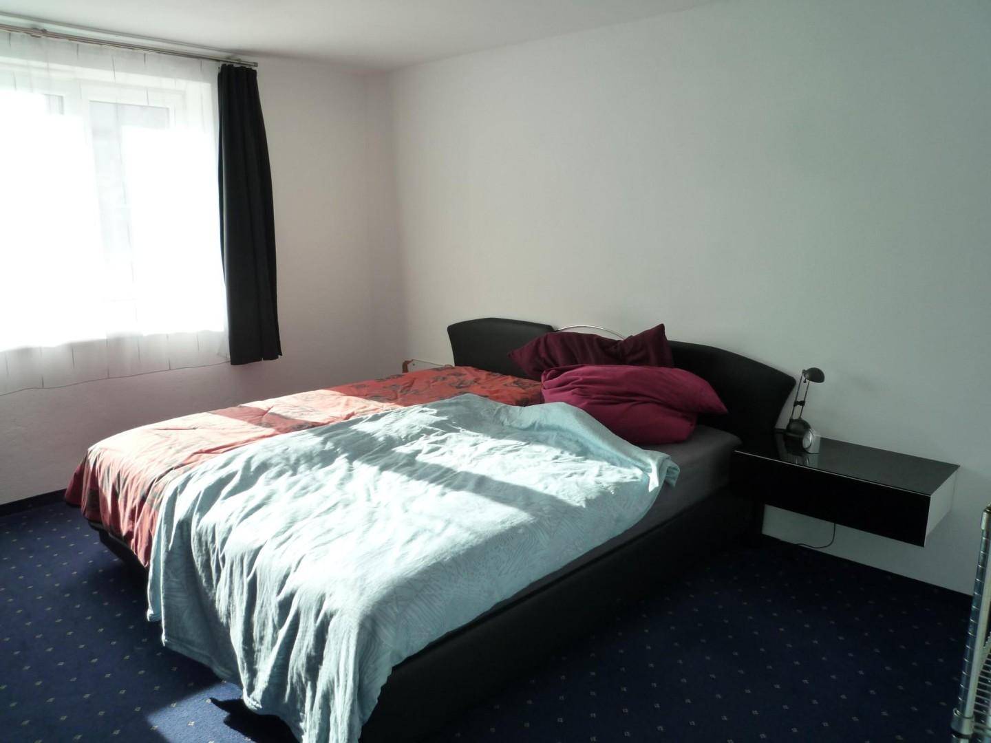 Schlafzimmer mit Doppelbett, Nachttischen und dunklem Teppichboden.