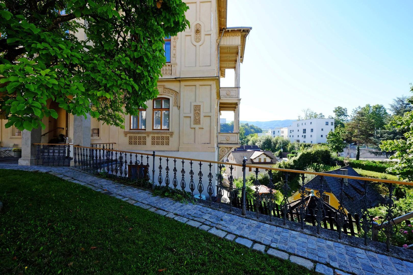 Seitenansicht der Villa mit gepflastertem Weg, Grünflächen und weitem Blick in die Landschaft.