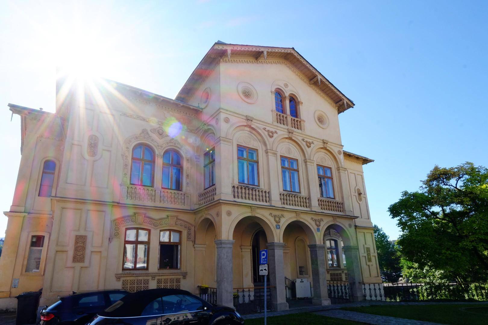 Sonnenbeschienene Fassade der historischen Villa mit architektonischen Details und blauem Himmel.