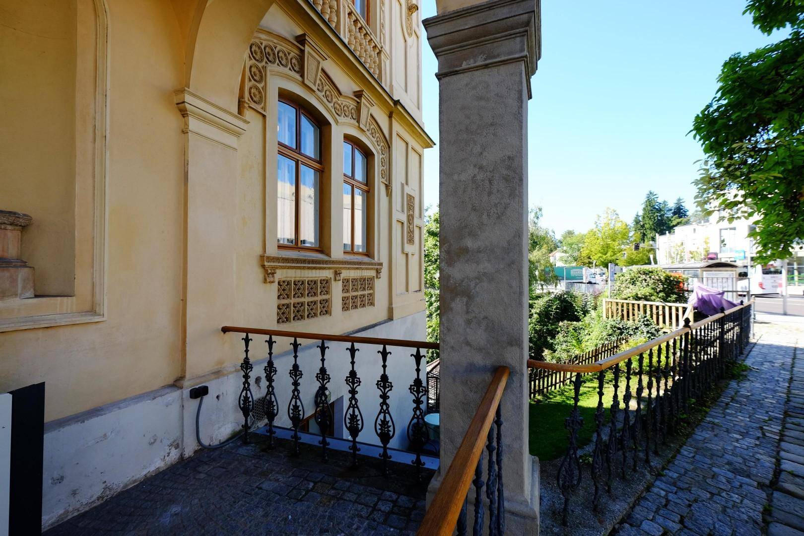 Historische Villa mit seitlichem gepflastertem Weg und schmiedeeisernem Geländer.