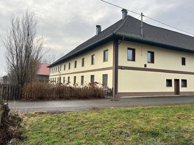 Lange Seite des traditionellen Gebäudes mit vielen Fenstern und dunklem Dach, umgeben von Natur.