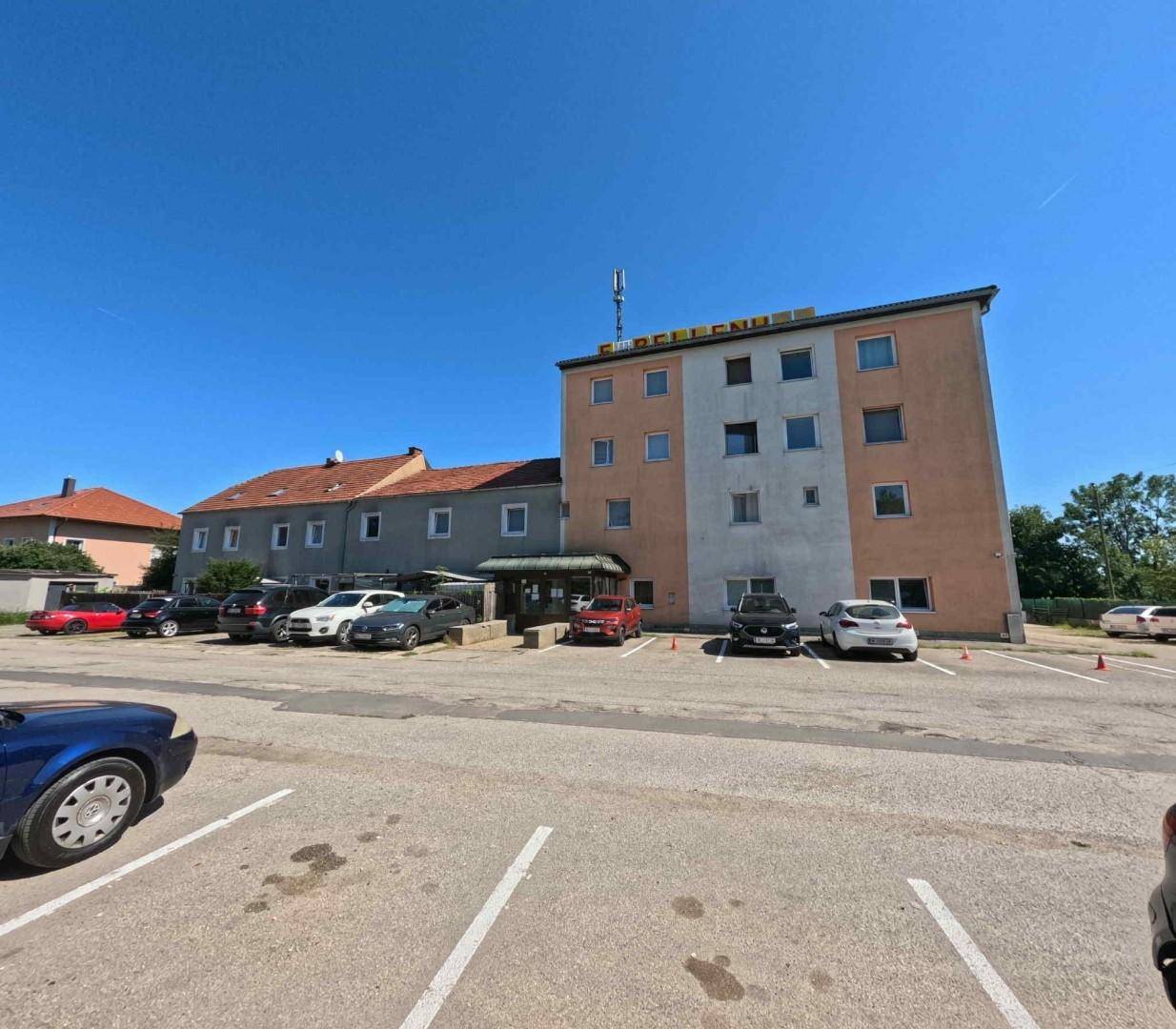 Außenansicht mehrerer Gebäude, darunter ein orange-weißes und ein graues, mit großem Parkplatz.