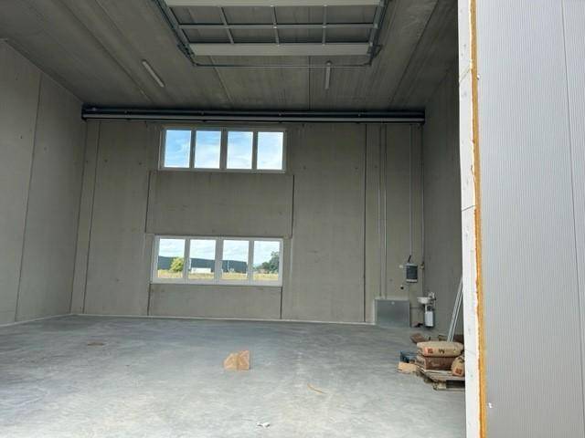 Geräumiger, leerer Innenraum einer Gewerbehalle mit Betonwänden, Betonboden und mehreren Fenstern, die Tageslicht hereinlassen.