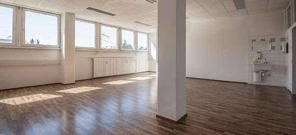 Offener Büroraum mit Laminatboden, einem tragenden Pfeiler und großen Fenstern für viel Licht.