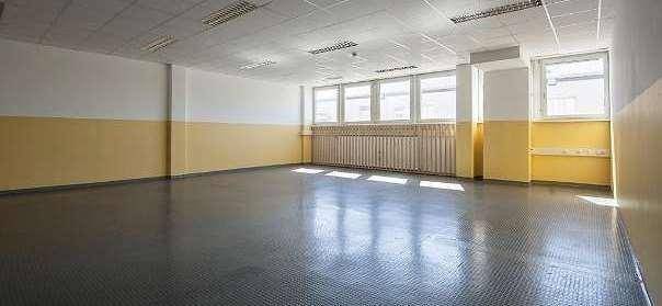 Großer Raum mit dunklem Boden, gelb-weißen Wänden und vielen Fenstern, die Tageslicht spenden.