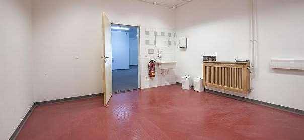 Kleiner Raum mit rotem Boden, Waschbecken und Heizkörper, möglicherweise ein Abstellraum oder eine Teeküche.