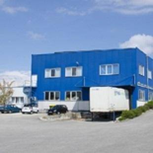 Blaues Industriegebäude mit Laderampe und einem LKW, umgeben von einem Parkplatz.