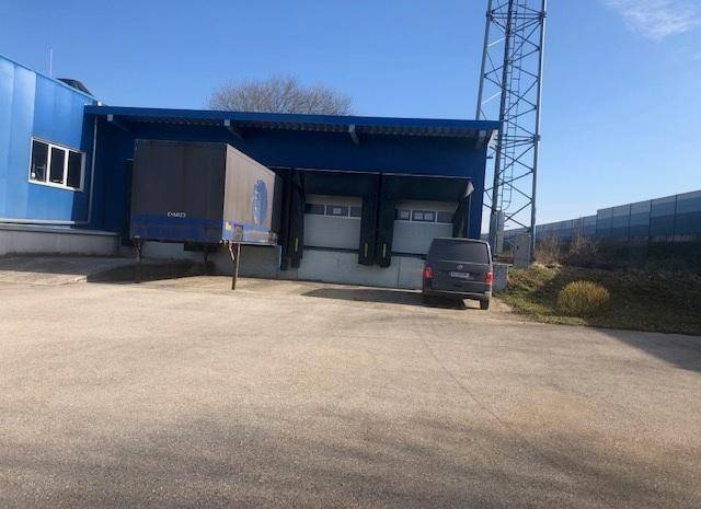Laderampenbereich des blauen Industriegebäudes mit zwei Toren und Fahrzeugen davor.