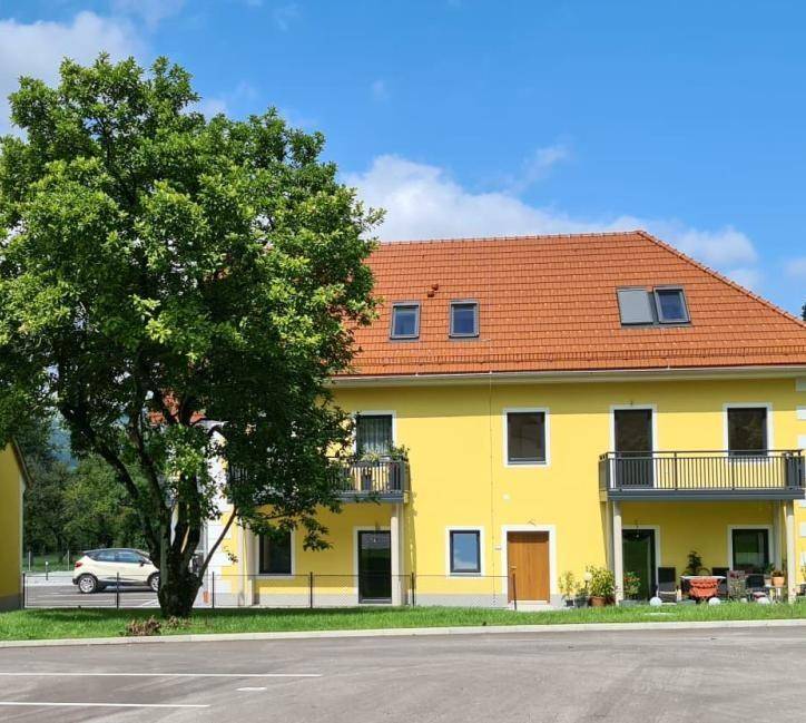 Gelbes Wohngebäude mit roten Ziegeldächern, Balkonen und einem großen Baum im Vordergrund.