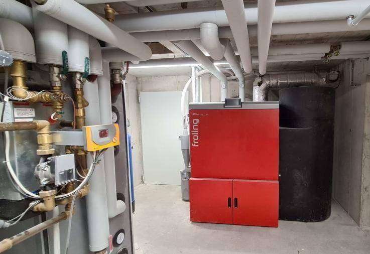 Heizungsraum im Keller mit einem roten Froling-Heizkessel und zahlreichen Rohren.