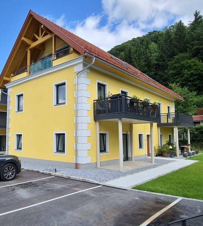 Modernes gelbes Gebäude mit Balkonen, weißen Akzenten und Blick auf bewaldete Hügel.