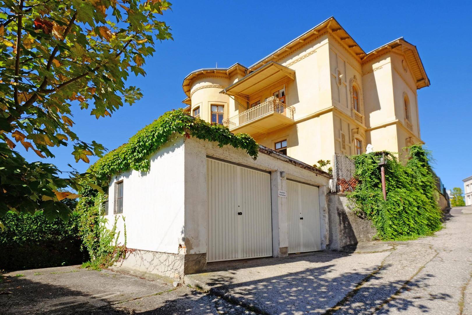Historische Villa mit separater Doppelgarage und üppiger Begrünung an der Fassade.