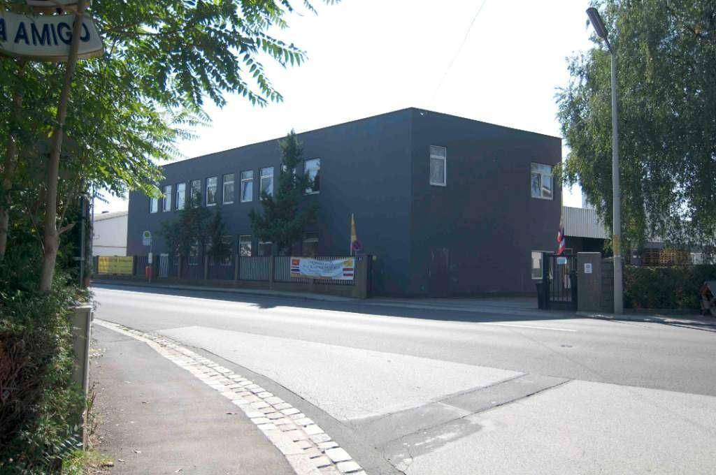Modernes Bürogebäude mit dunkler Fassade und großen Fenstern, umgeben von Bäumen an einer Straße.