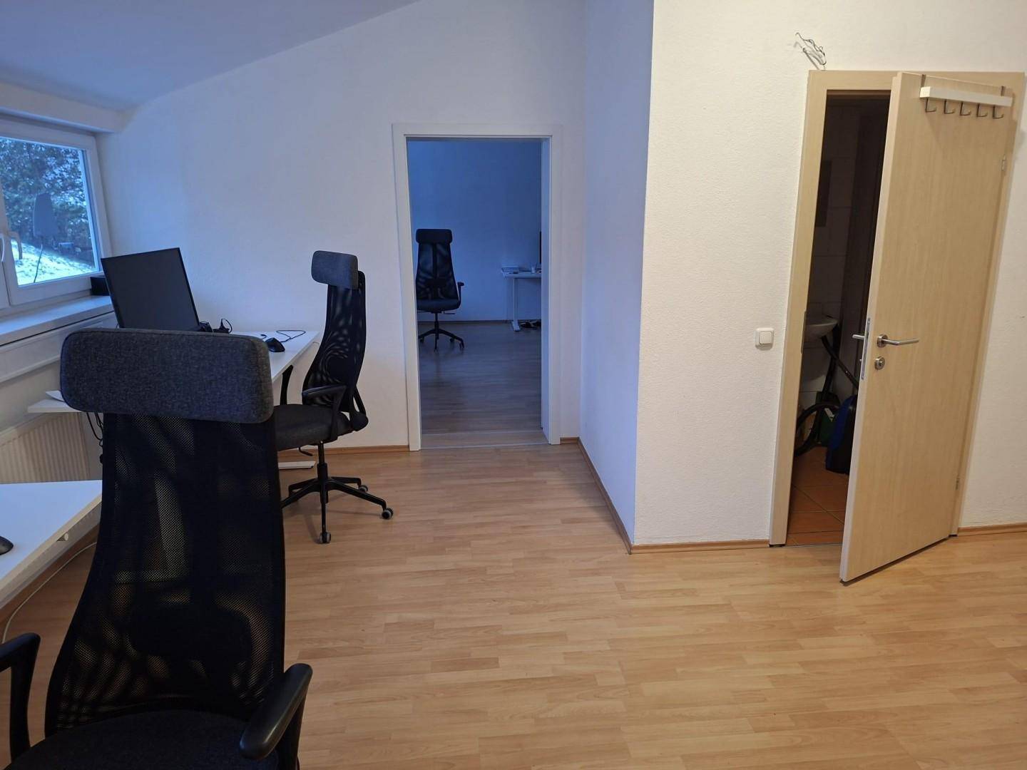 Büroraum mit hellem Laminatboden und Blick auf die verschneite Außenlandschaft durch ein Fenster.