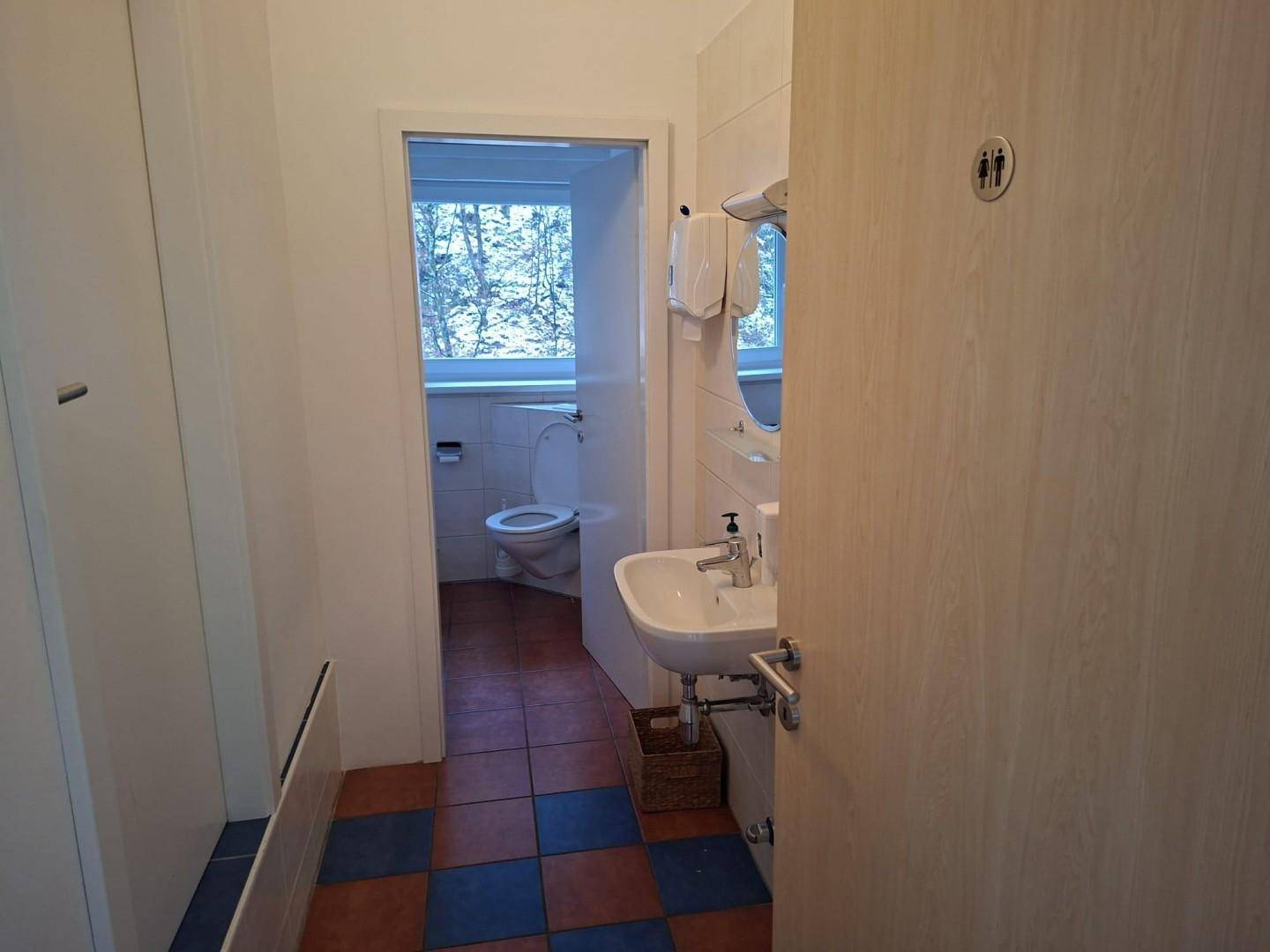 Badezimmer mit Waschbecken, Toilette und Fenster, gefliest in Blau und Terrakotta.