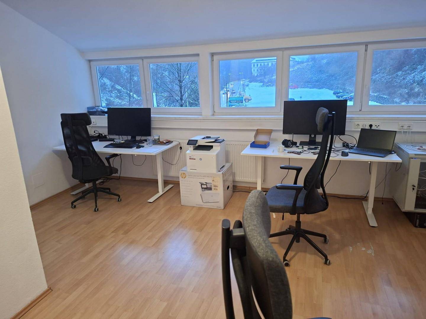 Moderner Büroraum mit zwei Schreibtischen, Computern und Blick auf die verschneite Landschaft.