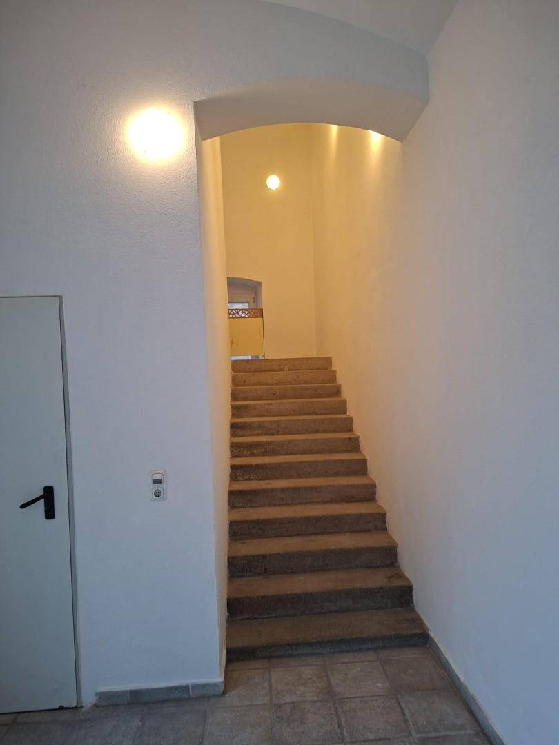 Heller Treppenaufgang mit Steinstufen und gewölbtem Durchgang, gut beleuchtet.