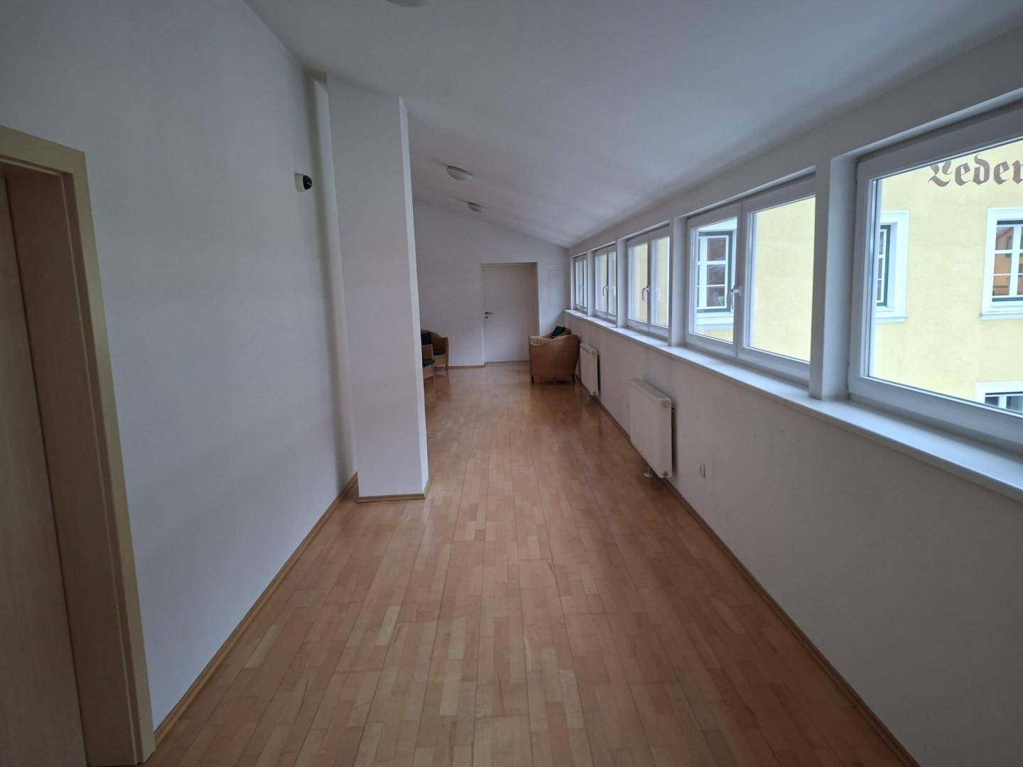 Langer Flur mit vielen Fenstern, die viel Tageslicht hereinlassen, und hellem Laminatboden.
