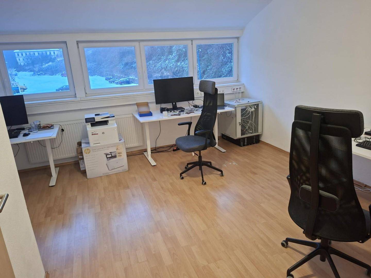 Heller Büroraum mit mehreren Arbeitsplätzen und Blick auf die verschneite Umgebung durch große Fenster.