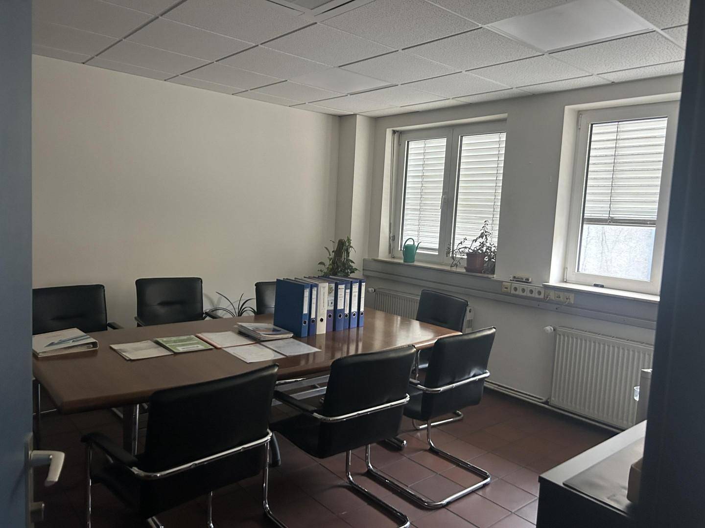 Besprechungsraum mit großem Holztisch, bequemen Stühlen und Aktenordnern, ideal für Teamtreffen und gut gepflegt.