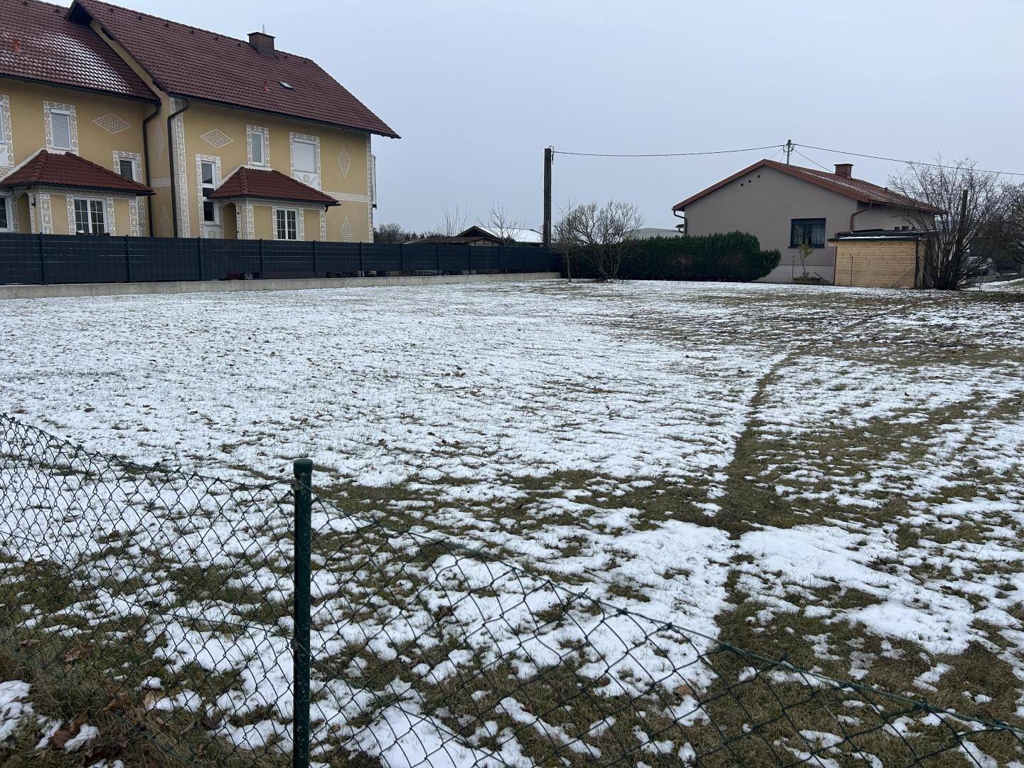 Weitläufiges Grundstück mit teilweiser Schneedecke und Blick auf benachbarte Häuser.