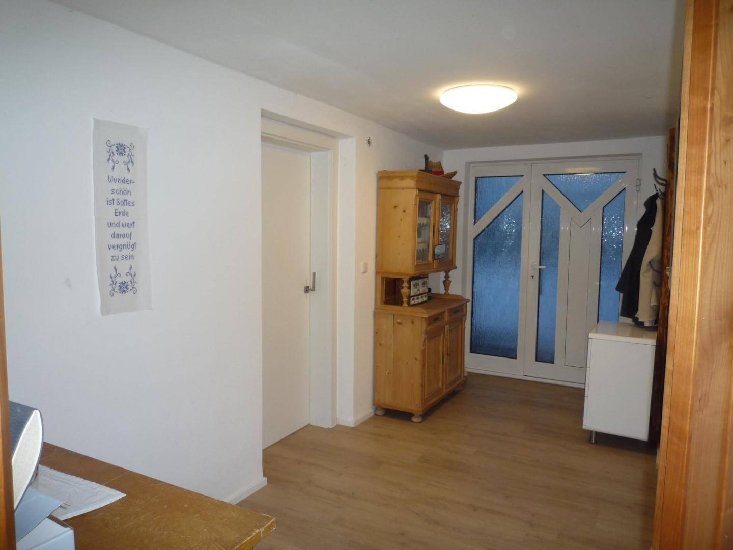 Heller Eingangsbereich mit Holzschrank, Garderobe und Glastür zum Außenbereich.