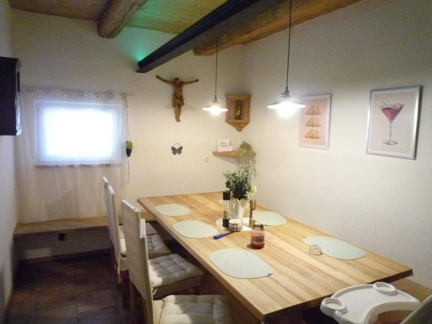 Gemütlicher Essbereich mit Holztisch, Bänken und traditioneller Dekoration an der Wand.