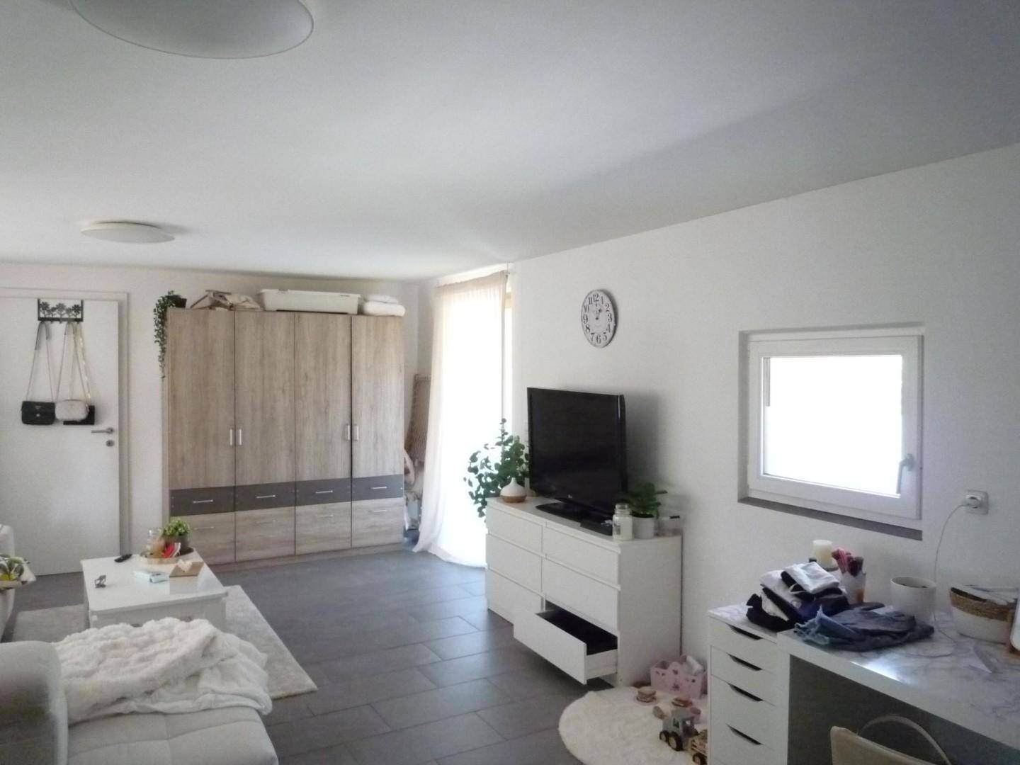 Helles Wohnzimmer mit Fliesenboden, großem Kleiderschrank und Zugang zum Balkon.