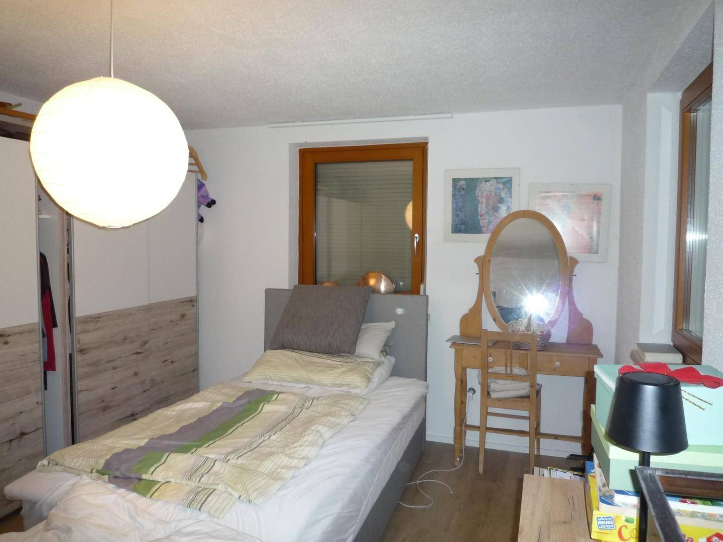 Schlafzimmer mit Einzelbett, Holzmöbeln und einem Schminktisch am Fenster.