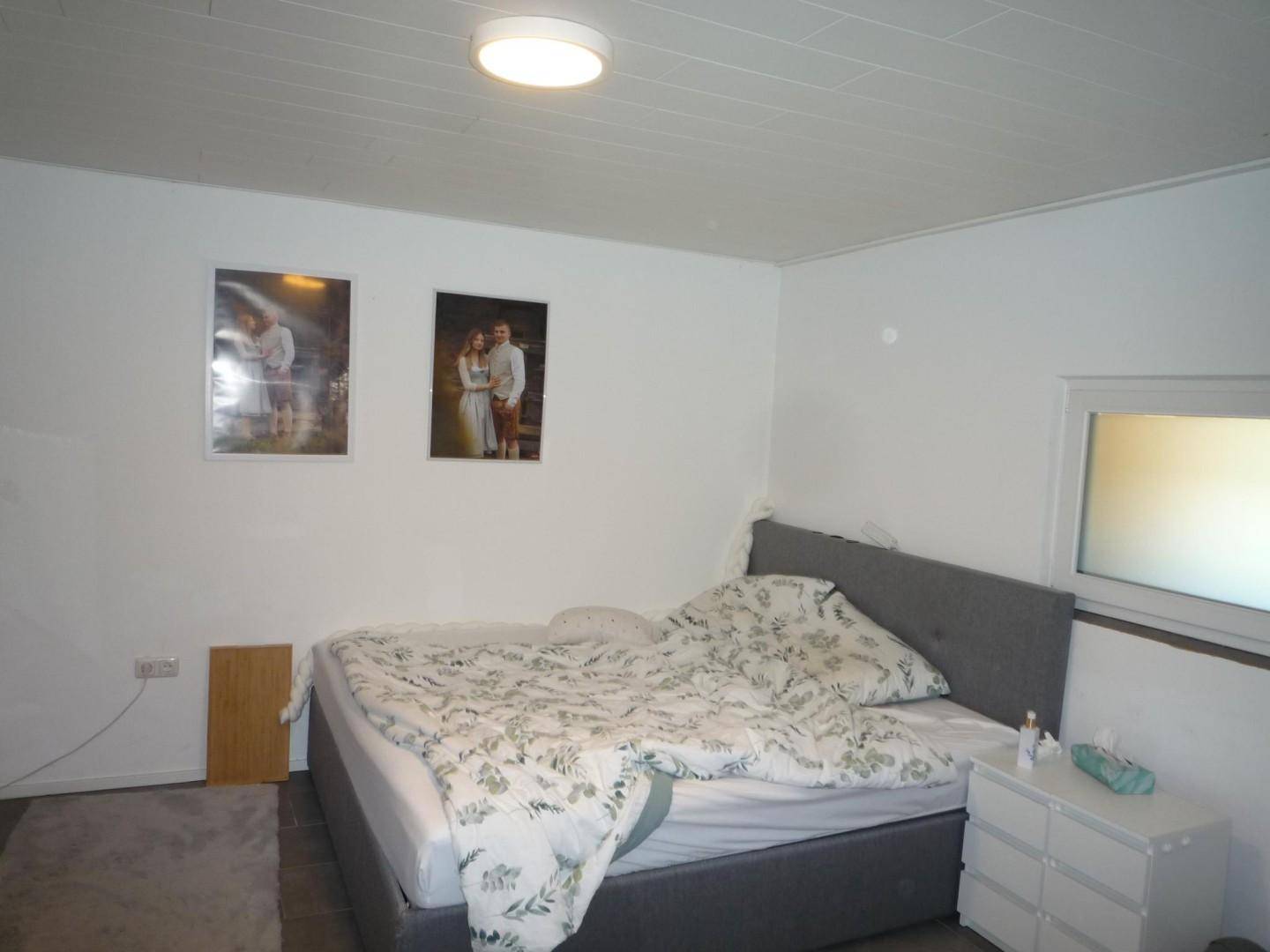 Schlafzimmer mit Doppelbett, schlichten Möbeln und einem Fenster für natürliches Licht.
