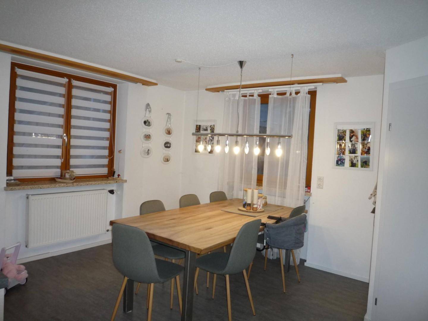 Moderner Essbereich mit Holztisch, grauen Stühlen und großem Fenster mit Jalousien.
