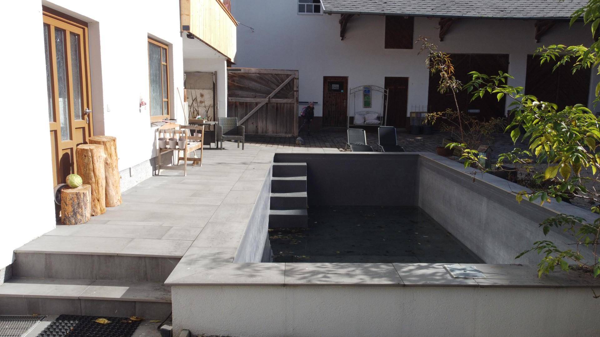 Unfertiger Poolbereich mit Treppen und angrenzender Terrasse, bereit für die Fertigstellung.