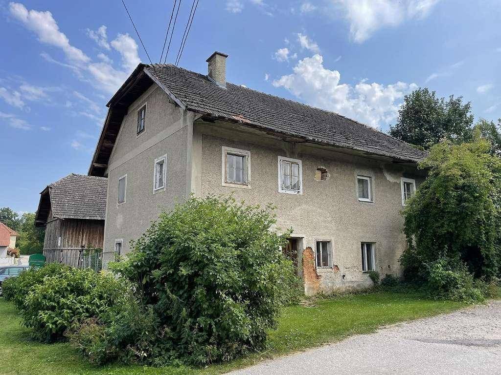 Altes Wohnhaus mit verputzter Fassade, kleinen Fenstern und einem Schornstein unter bewölktem Himmel.