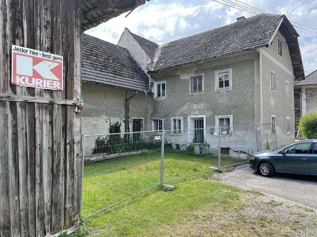 Gesamtansicht des alten Wohnhauses mit angrenzender Holzscheune und provisorischem Zaun.