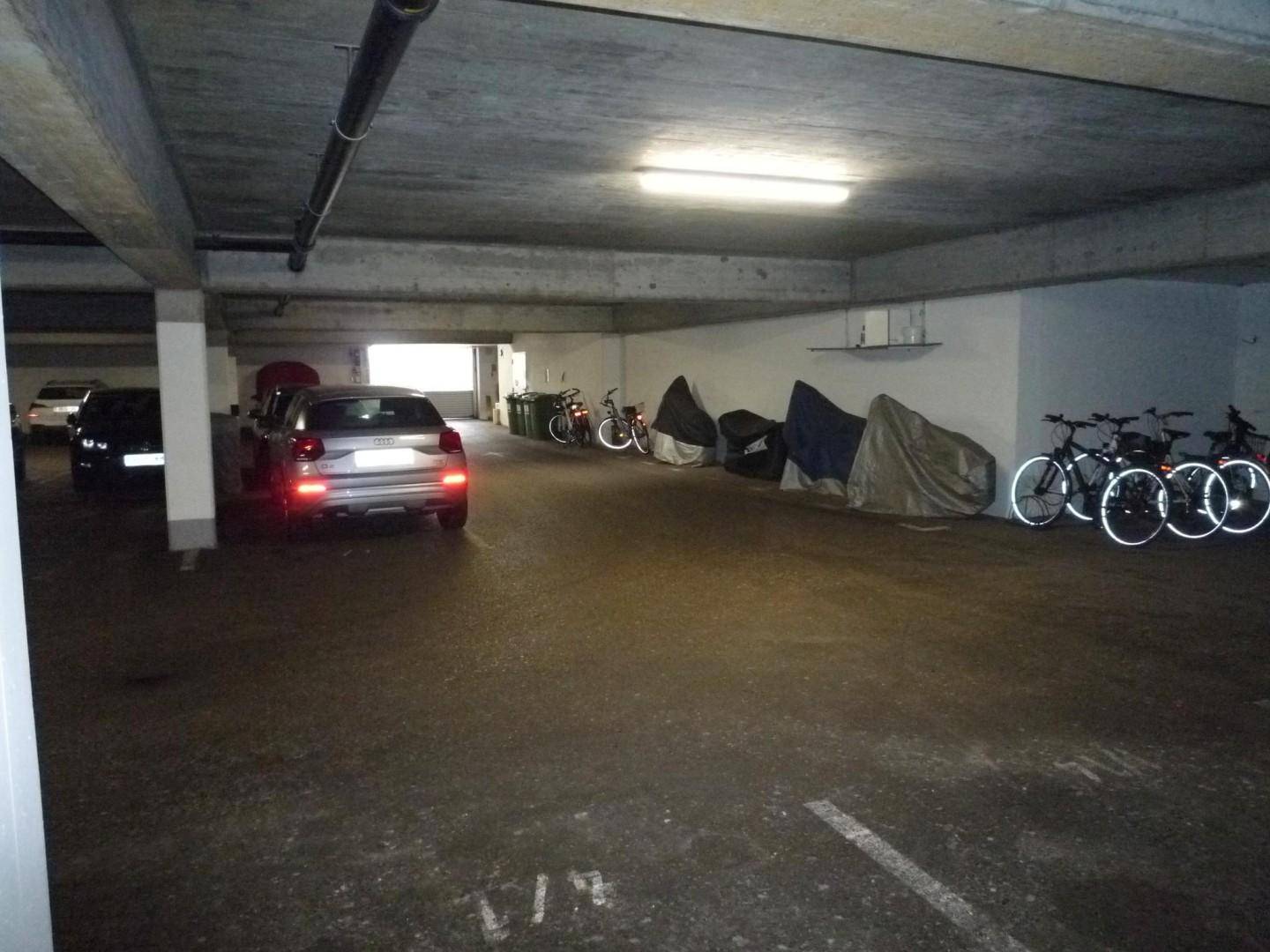 Tiefgarage mit parkenden Autos und Fahrrädern entlang der Wand.
