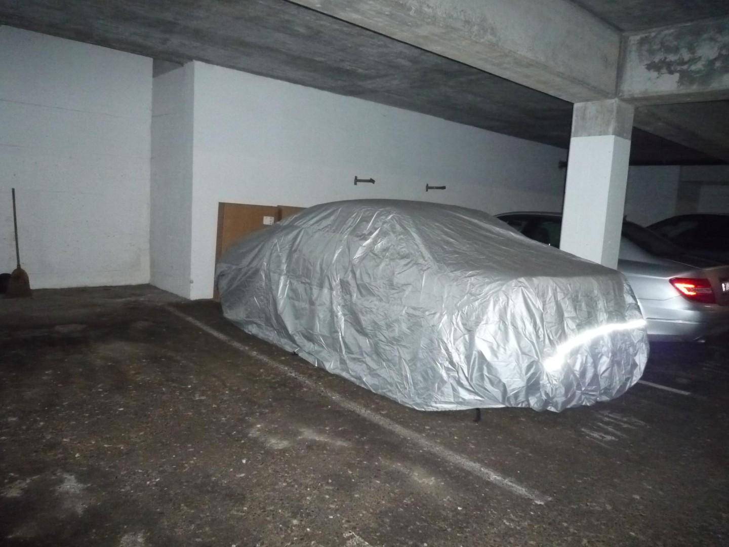 Tiefgarage mit einem abgedeckten Auto und sichtbaren Betonstrukturen.
