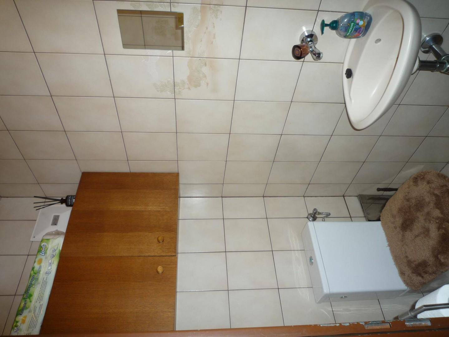 Kleines Badezimmer mit Toilette, Waschbecken und hellen Fliesen an Wänden und Boden.