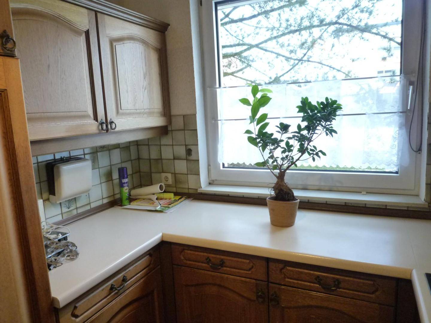 Küche mit hellen Arbeitsplatten, Holzschränken und einem Fenster über der Spüle.