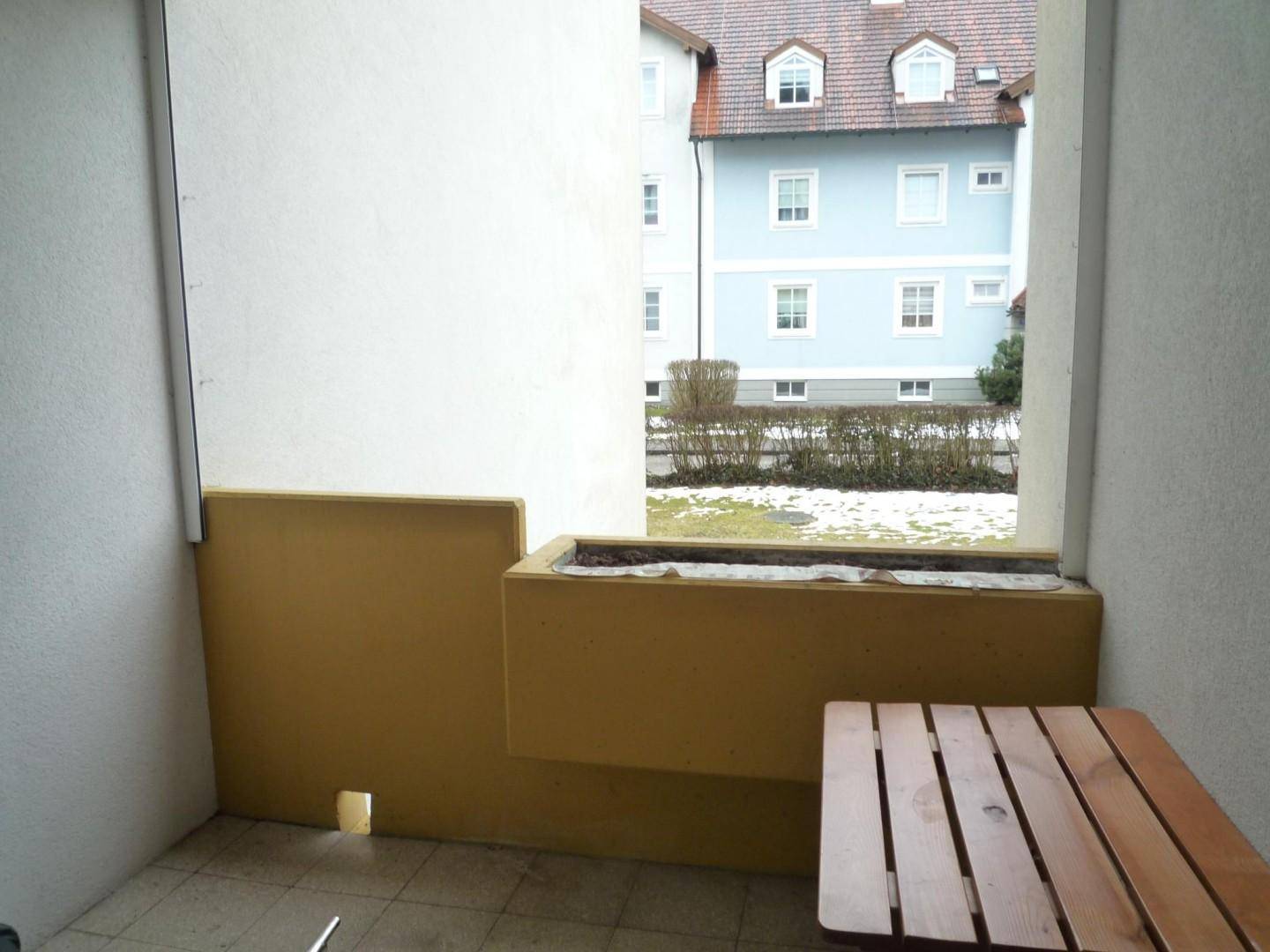Balkon mit kleinem Holztisch, Pflanzkasten und Blick auf ein gegenüberliegendes Gebäude.