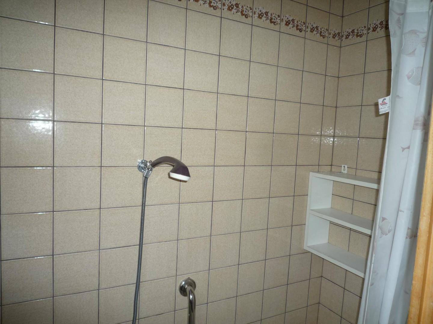 Duschbereich mit beigefarbenen Fliesen und einfacher Duscharmatur.