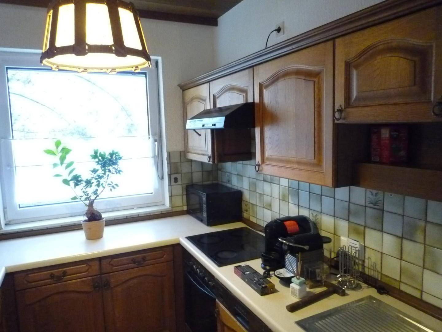 Funktionale Küche mit Holzschränken, Kochfeld und Kaffeemaschine unter einem Fenster.