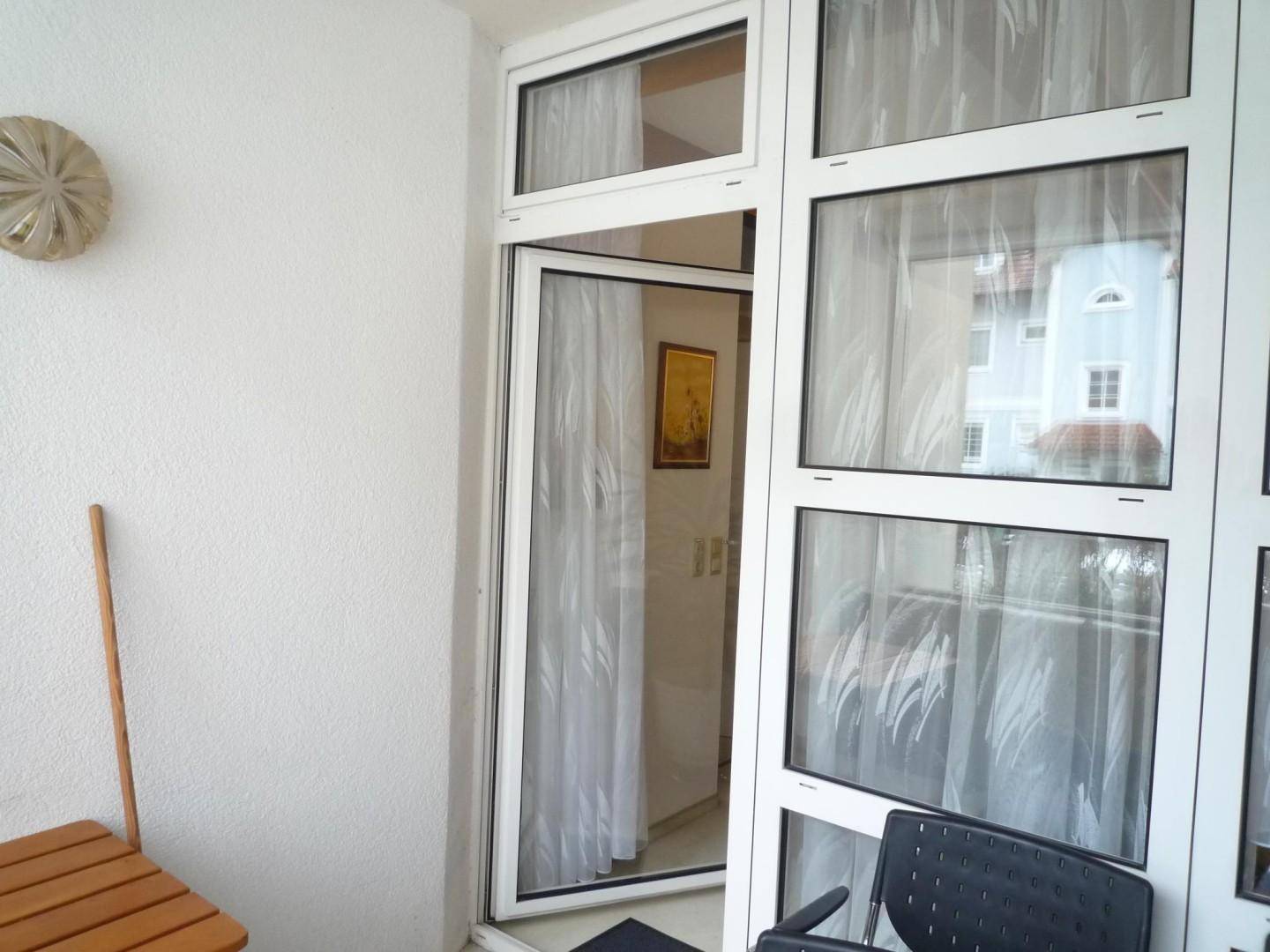 Balkon mit Glastür zum Innenbereich, kleinem Holztisch und einem Stuhl.